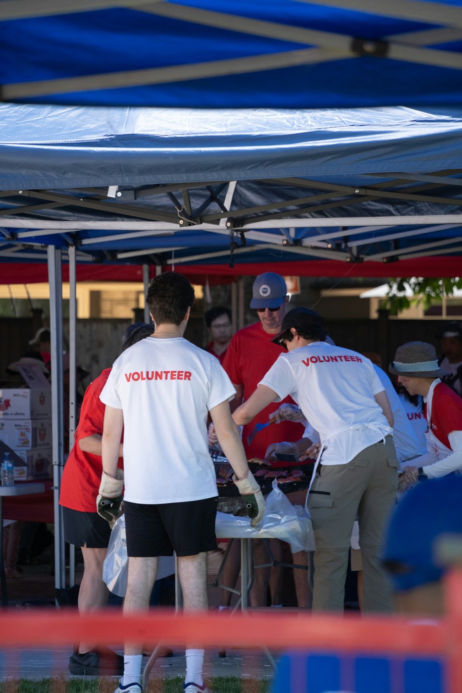 Volunteers in matching shirts serve food together beneath event tents.