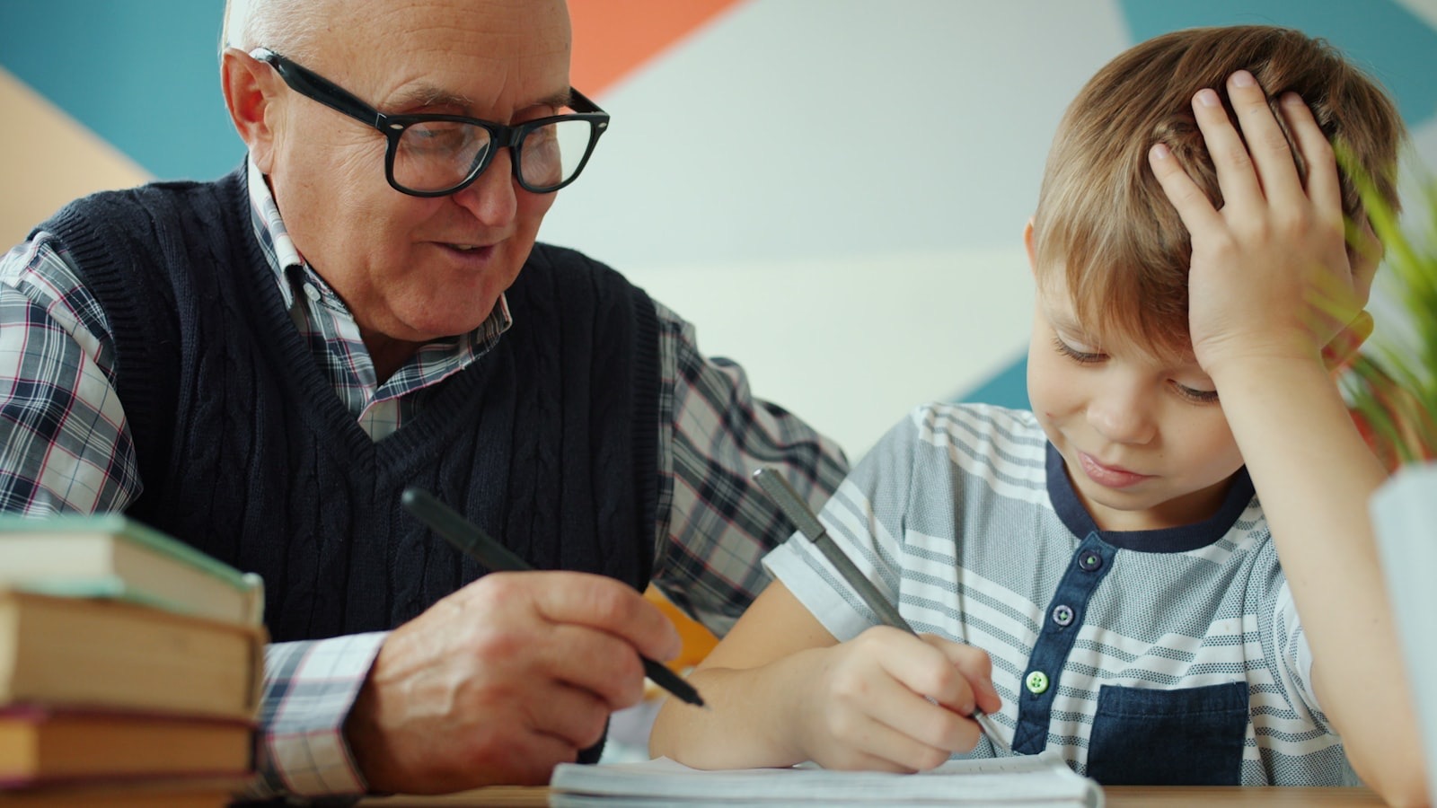 An older mentor helps a boy work through schoolwork at a table.