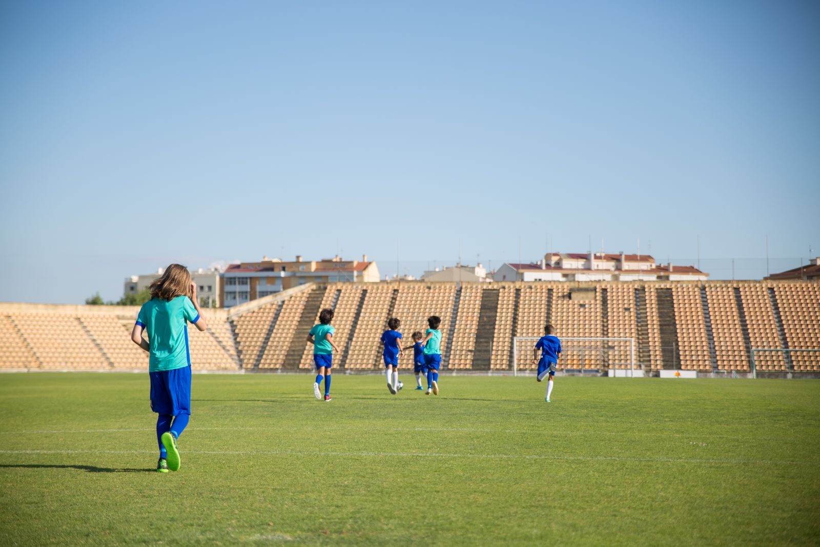 Young players run across a sunlit stadium soccer field.