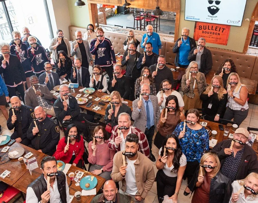 A large group of supporters packed into a restaurant, each holding a novelty moustache on a stick, at the Grow On Windsor campaign launch.