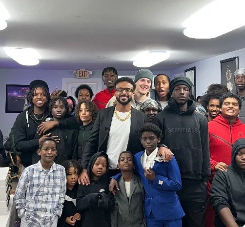 Mehari Hagos surrounded by a large group of young people from the MH100 programme indoors.