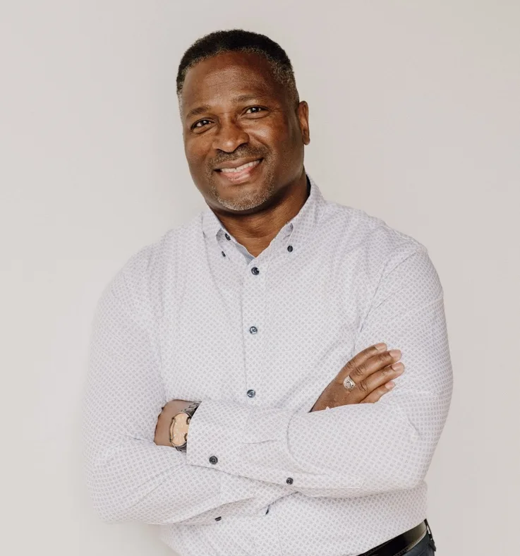 Des Griffiths, smiling with arms crossed, wearing a light patterned shirt.