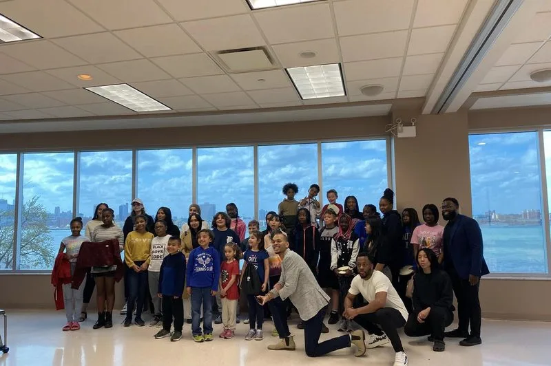 A large group of young people gathered by a wall of windows.