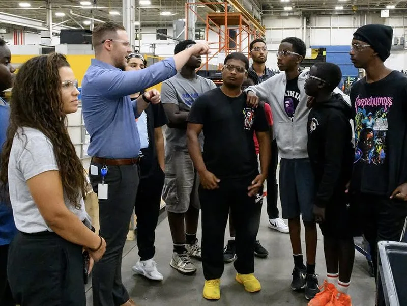 A group of youth and mentors gathered in a workshop space.