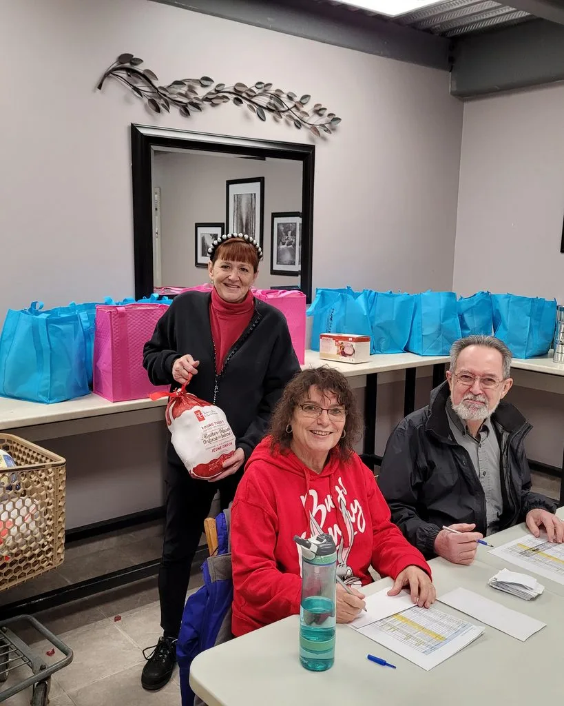 Three volunteers at a partner outreach centre, hampers and packed gift bags on the tables around them.