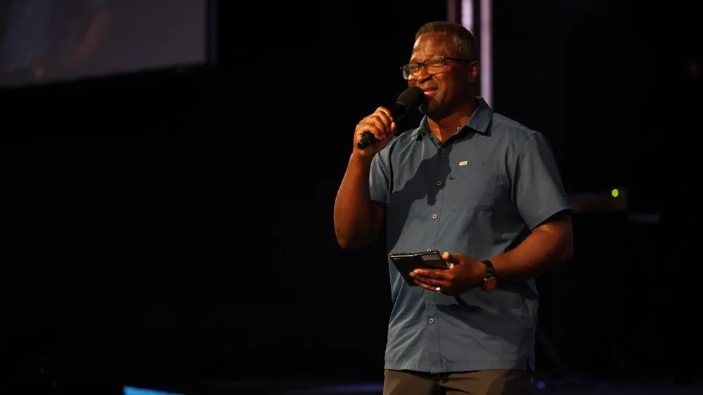 A speaker addressing a leadership session from the stage, microphone in hand.