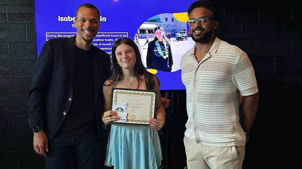 A student holding a framed award certificate, standing between two presenters.