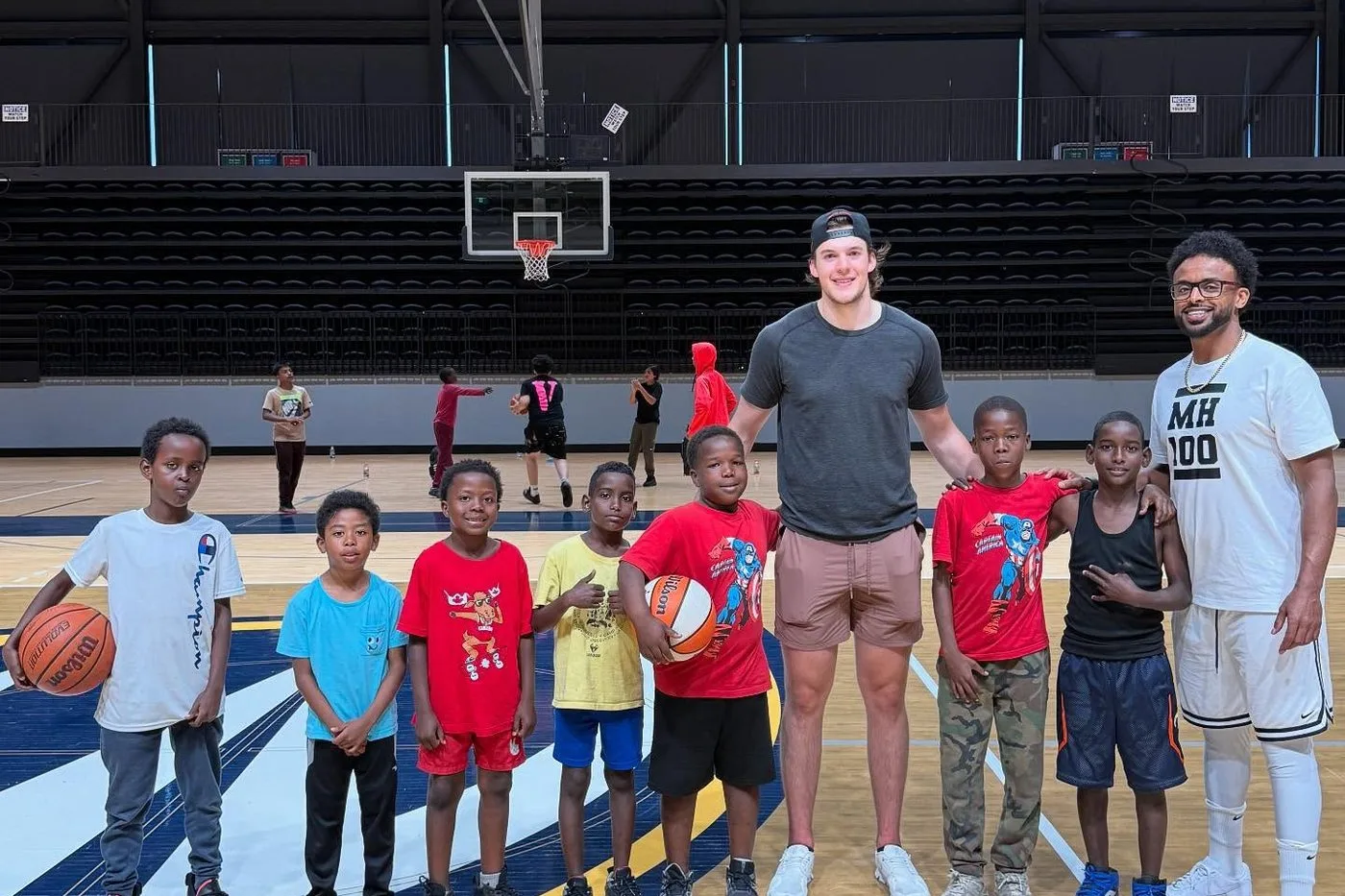 Two mentors standing with a group of young players on a basketball court after a session.